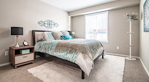 A bedroom with a queen sized bed and night stands. A large window with blinds