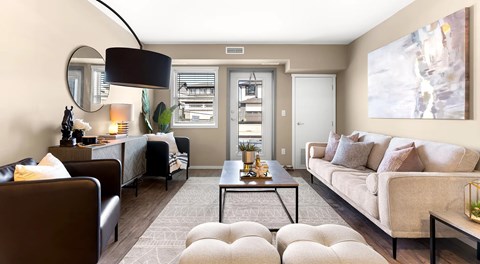 A living room with a large couch, a coffee table, and two arm chairs. A window sits next to a glass patio door