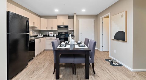 A kitchen with light cabinets and black appliances, a rectangular table sits in the centre