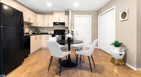 A kitchen with light cabinets and black appliances. A round table sitting in the centre with four chairs