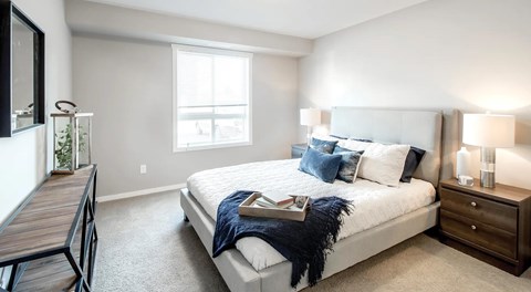 A bedroom with a queen sized bed, nightstands, and a window.
