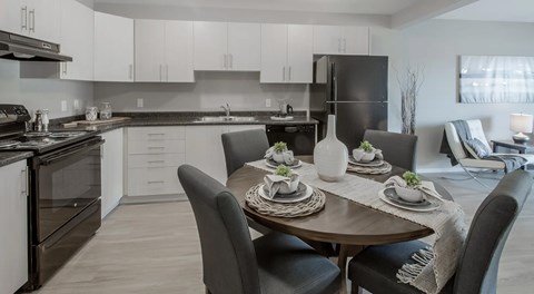 A bright open kitchen with light cabinets, dark counters and black appliances. A round table for four