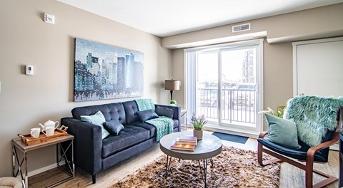 A living room with couch, end table, chair and coffee table. A large glass sliding door leading to a blacony