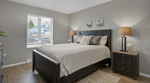 A bedroom with a large bed, a nightstand with a lamp, and a window with blinds.