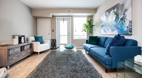 A living room with large couch, decorative display stand and chair. a patio door and large window sit on the exterior wall
