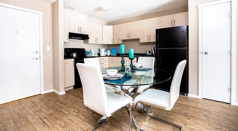 A bright kitchen with light cabinets and black appliances. A small pantry and round table