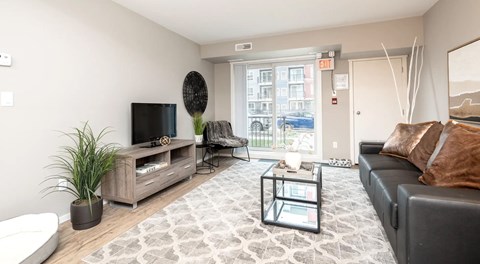 a spacious living room with couch, chairs, coffee table and tv with stand. Glass sliding door and utility closet