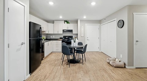 A white kitchen, with light cabinets and black appliances a round kitchen table set for four
