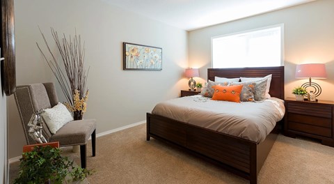 A bedroom with a bed, nightstand, chair, and lamp.