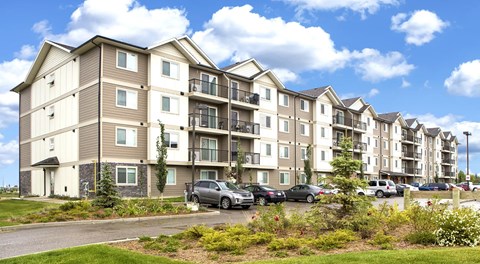 A row of apartment buildings with cars parked in front.