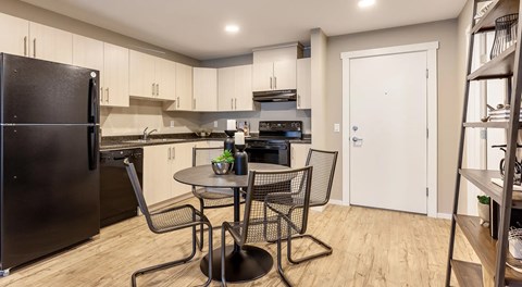 A kitchen with light cabinets and black appliances, a round table sits centre with four chairs around it