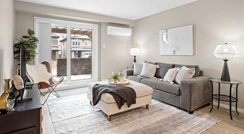A living room with a grey couch, a white chair, and a table with a lamp on it.