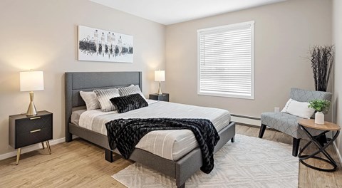 A bedroom with a large bed, a nightstand, a chair, and a painting on the wall.
