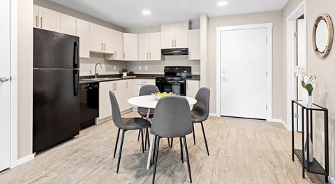 A kitchen with a black fridge, white cabinets, a table with four grey chairs, and a white door.
