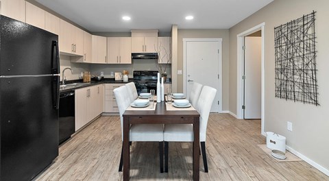 A bright kitchen with light cabinets and black appliances, a rectangular table set for four in the centre
