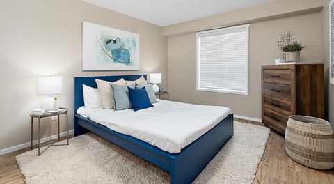 A bedroom with large bed, night stands, a dresser and basket next to a window with blinds