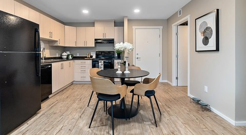 A kitchen with light cabinets and black appliances. A round kitchen table with four chairs sits in the centre