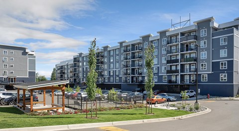 A mordern apartment complex with lots of parking in front with a pergola and dog run