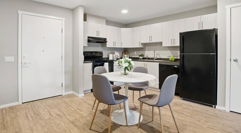 A kitchen with light cabinets and black appliances. A small pantry sits next to the fridge and a round kitchen table in the center of the room.