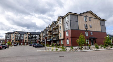 A row of apartment buildings with cars parked in front.