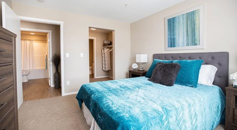 A bedroom with queen sized bed, night stands and a dresser. A walk in closet leading to an ensuite