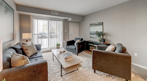 A open living room with a couch, coffee table and two chairs. A large sliding door with lots of natural light