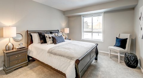 A large bedroom with queen sized bed, night stands a chair and big window