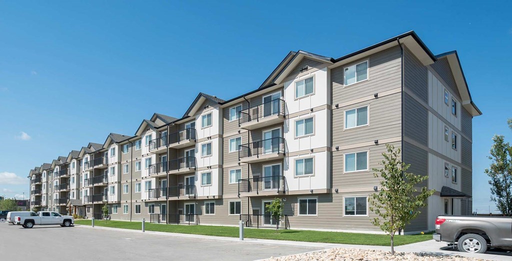 A row of modern apartment buildings with cars parked in front.
