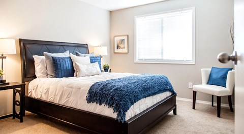 a bedroom with queen sized bed, night stands a chair and large window