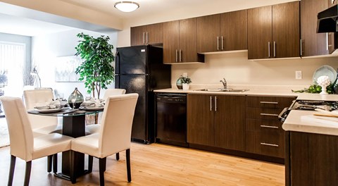 a large open kitchen with dark cabinets, light countertops and black appliances. A round table set for four in the centre of the room