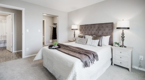 A bedroom with a queen sized bed, a nightstand, and an entrance to a walk in closet