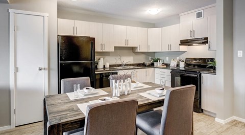 A open modern kitchen with light cabinets, black appliance and table set for four