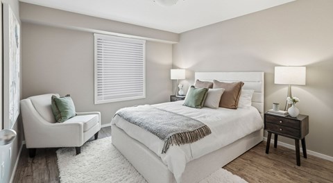 A bedroom with queen sized bed, night stands and chair. A big window with blinds