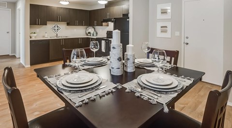 A kitchen with dark cabinets, light counters and black appliances. A kitchen table set for four