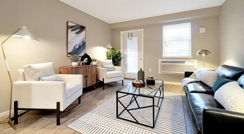 A living room with couch, chairs, coffee table. A patio door, window and AC unit on outer wall