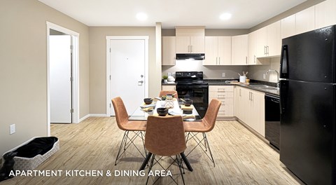 Apartment kitchen with light cabinets, black appliances and a rectangular table in the centre