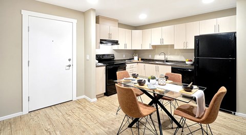 Bright open kitchen with light cabinets, black appliances and a rectangular table set for four