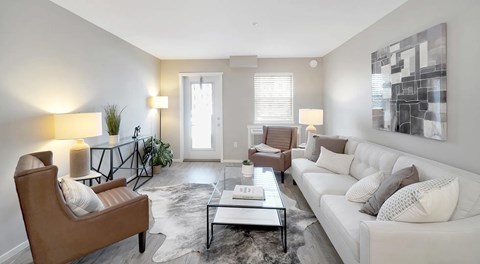 A living room with a couch, chairs and coffee table. A window sits next to a patio door