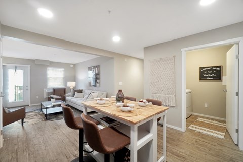 A dining room with a table set for two and a couch in the background.