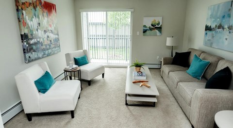 A living room with a large couch, coffee table and two arm chairs sit next to a large glass sliding door