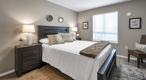 A bedroom with a large bed, a nightstand with a lamp, and a chair.