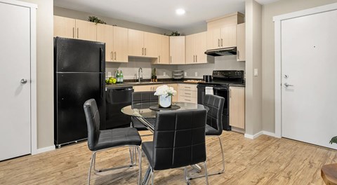 An open concept kitchen with black appliance and light cabinets. A table for four sits in the middle