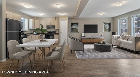 An open concept townhome with light kitchen cabinets, black appliances and rectangular table off to the side. A small pantry separates the two spaces with an open living room with two large windows on the other side