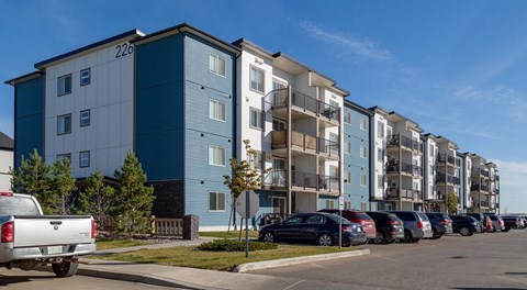 A row of apartment buildings with cars parked in front.