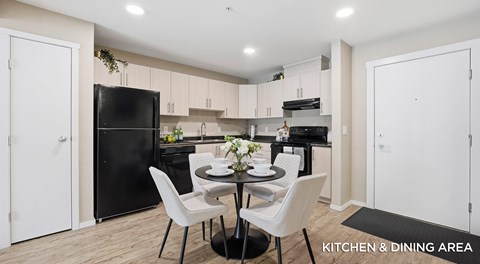 A modern kitchen and dining area with a black fridge, white chairs, and a table set for two.