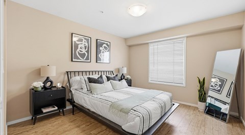 A bedroom with a large bed, two nights stands and floor length mirror. A large window with blinds  is against one wall