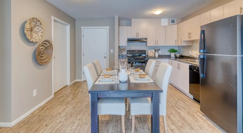 A modern kitchen with light cabinets, black appliances and a rectangular dining table with four chairs