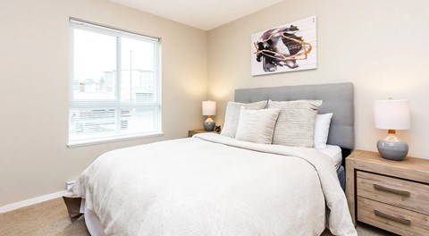 A bedroom with a large bed, two lamps, and a painting on the wall.
