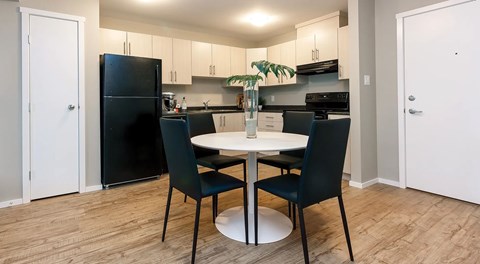 An open kitchen with light cabinets and black appliances. A round table with four chairs in the center and pantry door