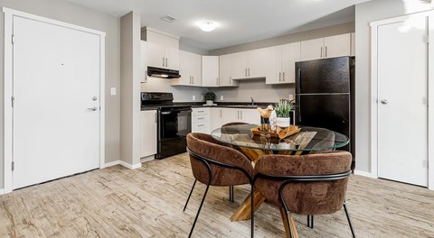 A modern open kitchen with light cabinets and black appliances, a round table sits in the centre